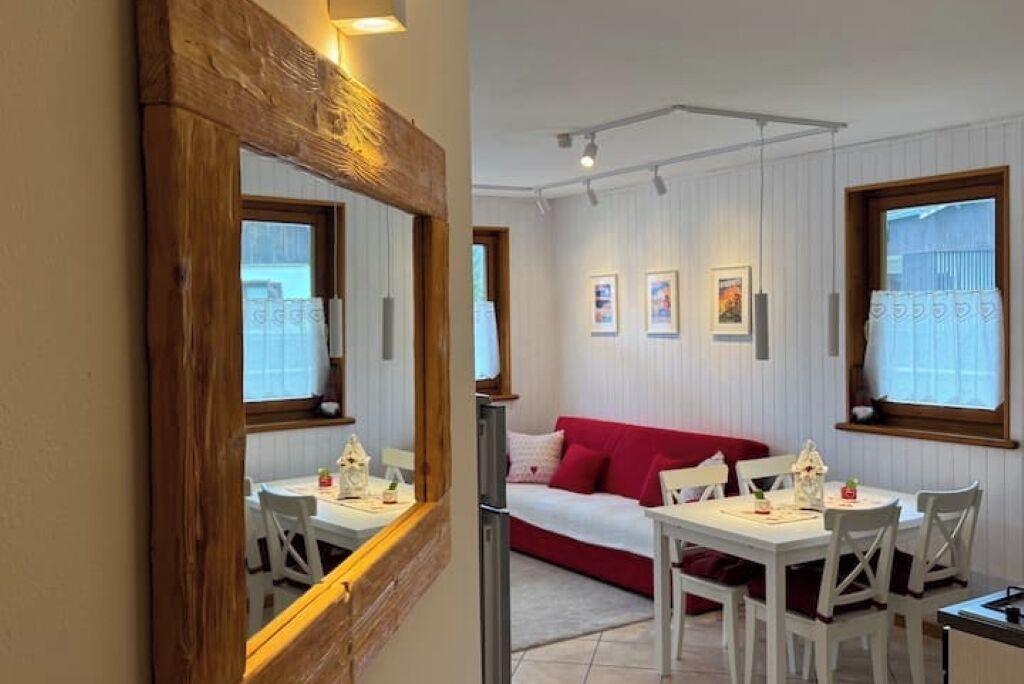 Ein Essbereich mit einem spiegelnden Wandbild aus Holz, einem weißen Tisch und Stühlen, einem roten Sofa im Hintergrund und gerahmten Bildern an der Wand.