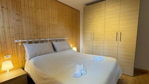 Ein Schlafzimmer mit einer Holzwand, einem großen Bett mit weißer Bettwäsche, zwei Nachttischlampen und einem zweitürigen Kleiderschrank.