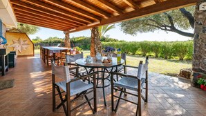 Eine Terrasse im Freien mit Holztischen und -stühlen, einer Steinsäule und Blick auf einen Weinberg.