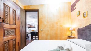 Ein Hotelzimmer mit einem Bett, einer Holztür mit aufwendigen Schnitzereien, einem Essbereich im Hintergrund und einer Wandleuchte.