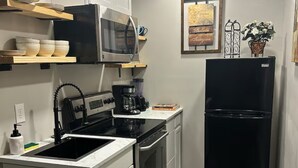 Una cucina compatta con mobili bianchi, un forno a microonde, un piano cottura, un lavello e un frigorifero nero.