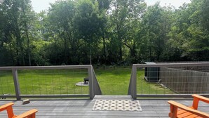 A deck with two orange chairs, a small table, and a view of a grassy yard with a wooden fence and trees.