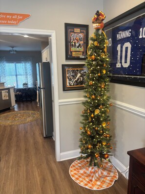 Un árbol de Navidad decorado en una sala de estar con recuerdos deportivos enmarcados en la pared.
