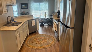 A modern kitchen with white cabinets, stainless steel appliances, a round rug, and a dining area with a table and chairs.