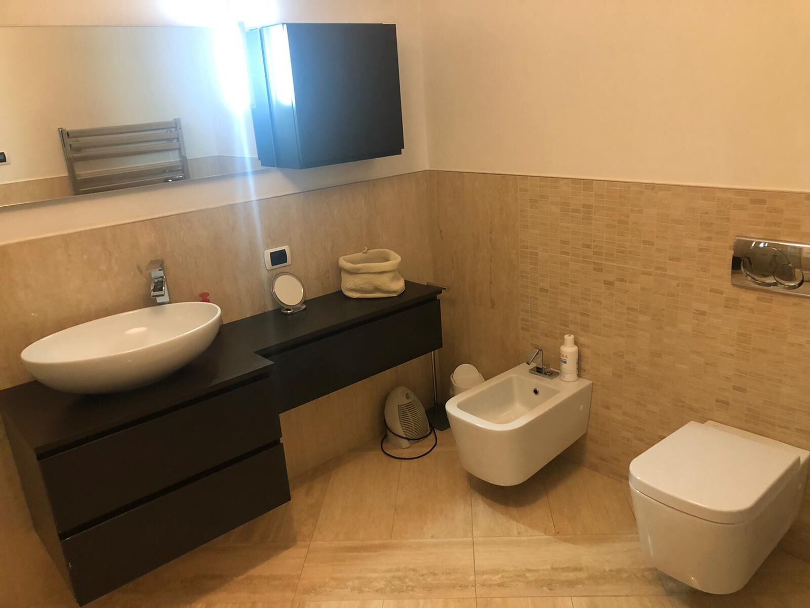 Une salle de bain moderne avec un grand lavabo blanc, un bidet, des toilettes, un miroir et un porte-serviettes.