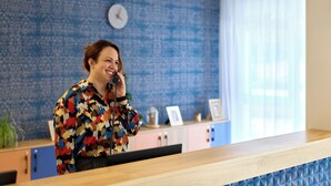 A reception desk with a patterned wall and a clock in the background. - Quality Aparthotel Saint-Paul-lès-Dax (Saint-Paul-lès-Dax)