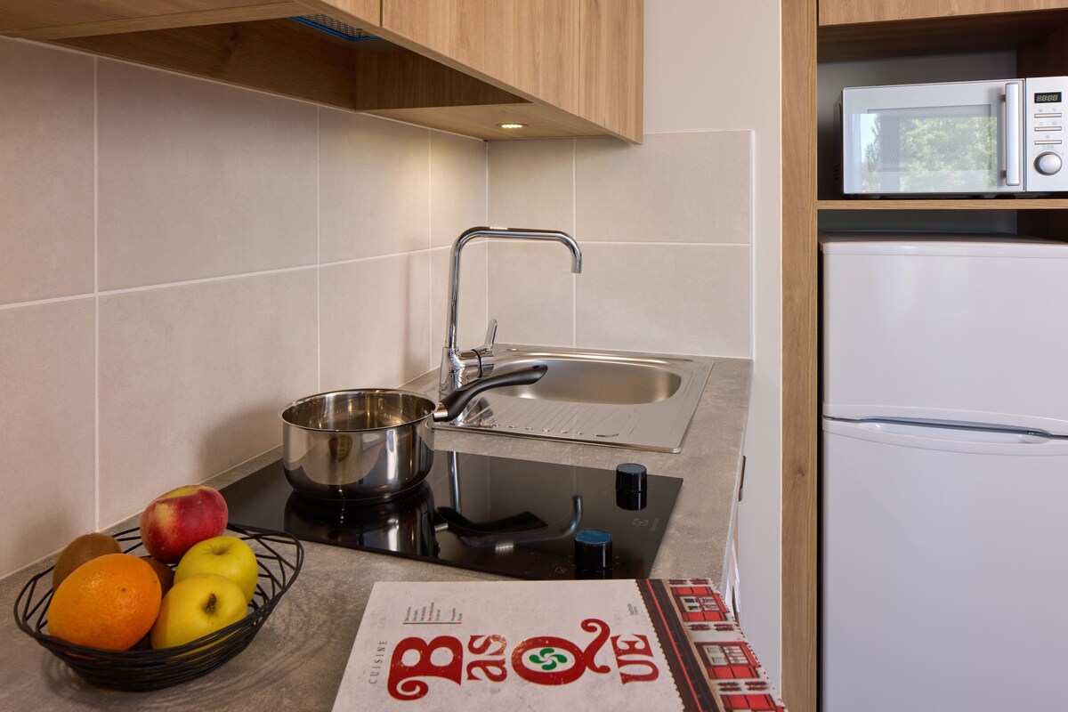 A kitchen with a sink, stove, and microwave. There is a bowl with fruits and a menu on the counter.