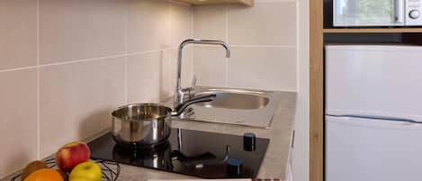 A kitchen with a sink, stove, and a microwave. There is a bowl with fruits and a menu on the counter.