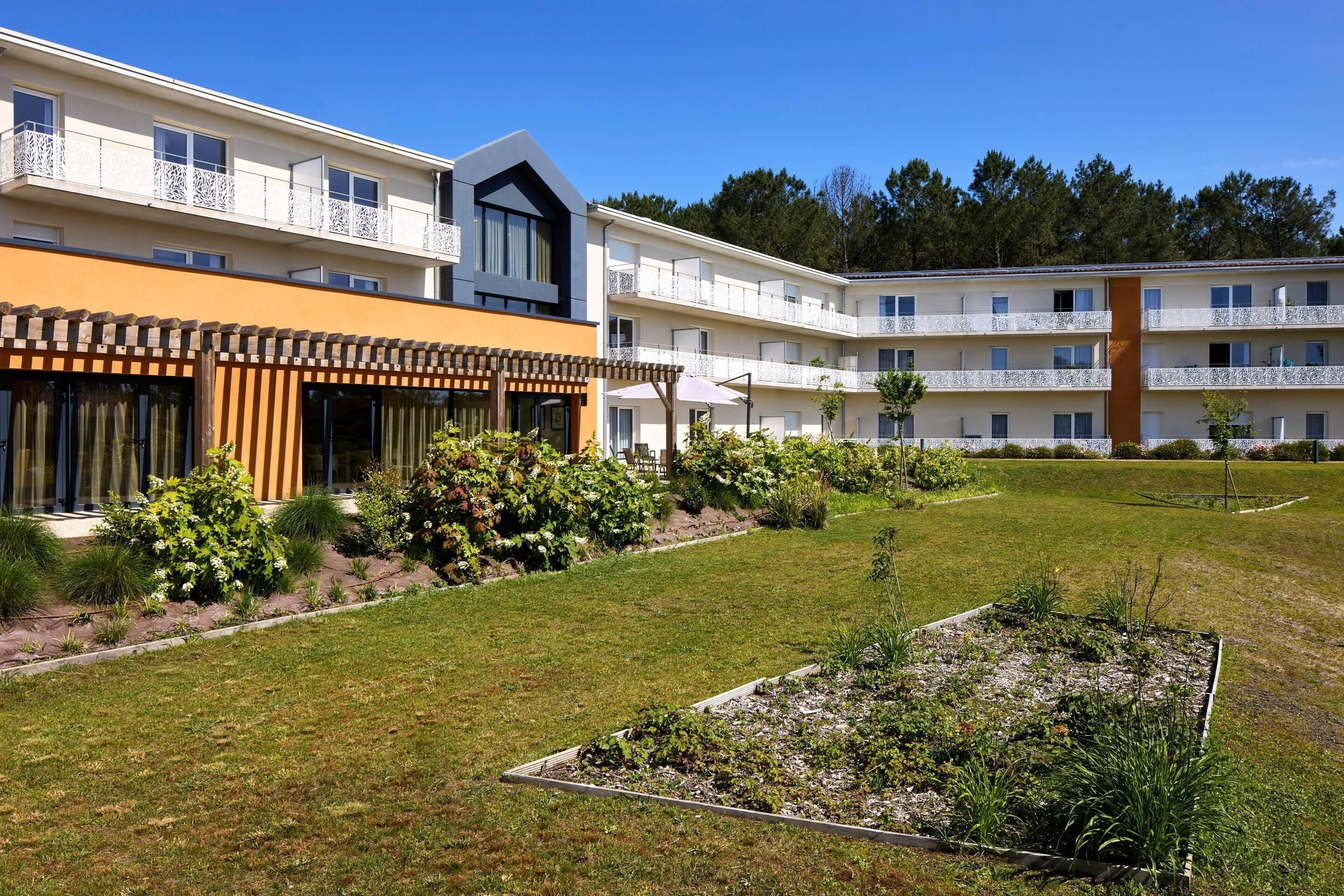 Un hôtel moderne doté de nombreux balcons, d’un jardin bien entretenu et offrant une vue sur un ciel d’un bleu éclatant.