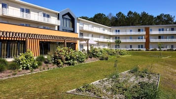Un hotel moderno con varios balcones, un jardín cuidado y un cielo azul despejado.