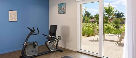 A home gym with an exercise bike, two yoga mats, and a large sliding glass door leading to a patio with outdoor furniture.