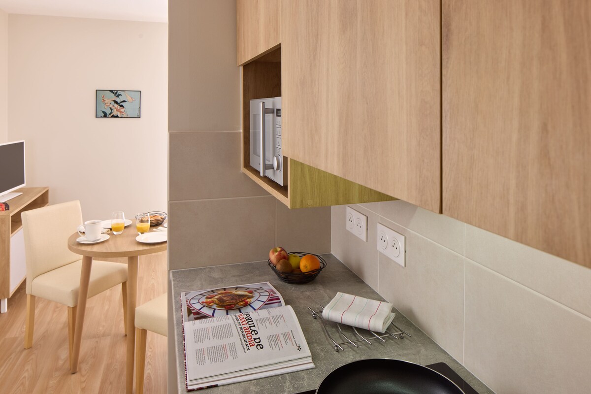 A modern kitchen with wooden cabinets, a dining area with a table and chairs, and a fruit bowl.
