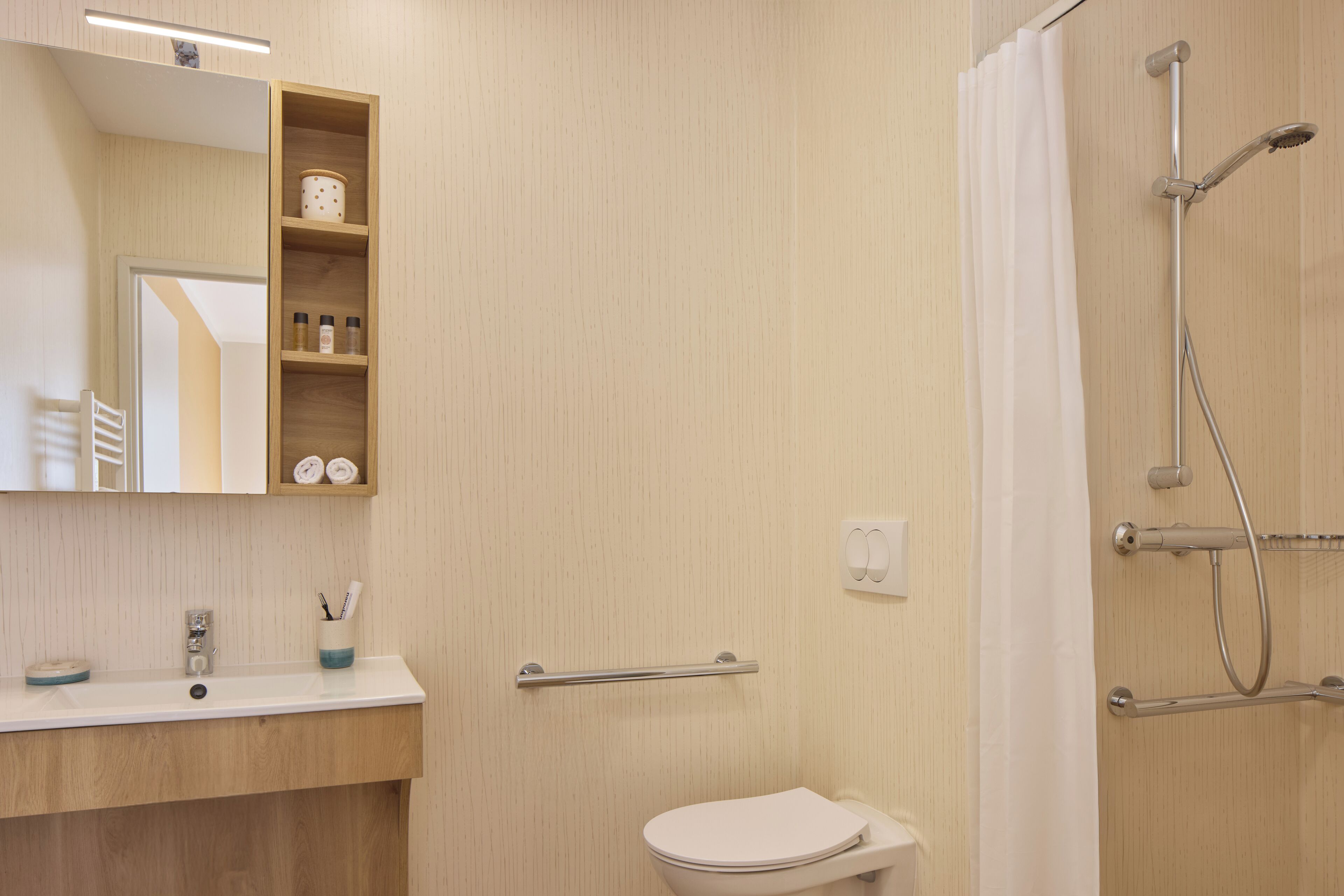 A bathroom with a wooden vanity, a toilet, a shower with a handheld showerhead, and a mirror above the vanity.
