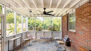 A sunroom with a ceiling fan, large windows, a hanging chair, and a patterned rug. - Charming Home East Nashville (Nashville)