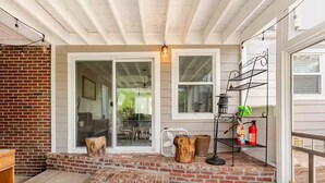 A covered porch with a brick step leading to a sliding glass door, a metal rack with cleaning supplies, and a fire extinguisher. - Charming Home East Nashville (Nashville)