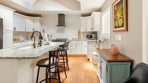 A modern kitchen with white cabinets, a marble island, bar stools, a microwave, and a painting on the wall. - Charming Home East Nashville (Nashville)