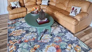 A tan leather sectional sofa with decorative pillows, a green coffee table with books and a lantern, and a floral-patterned rug. - Charming 1-bedroom country getaway in serene Salisbury (Salisbury)