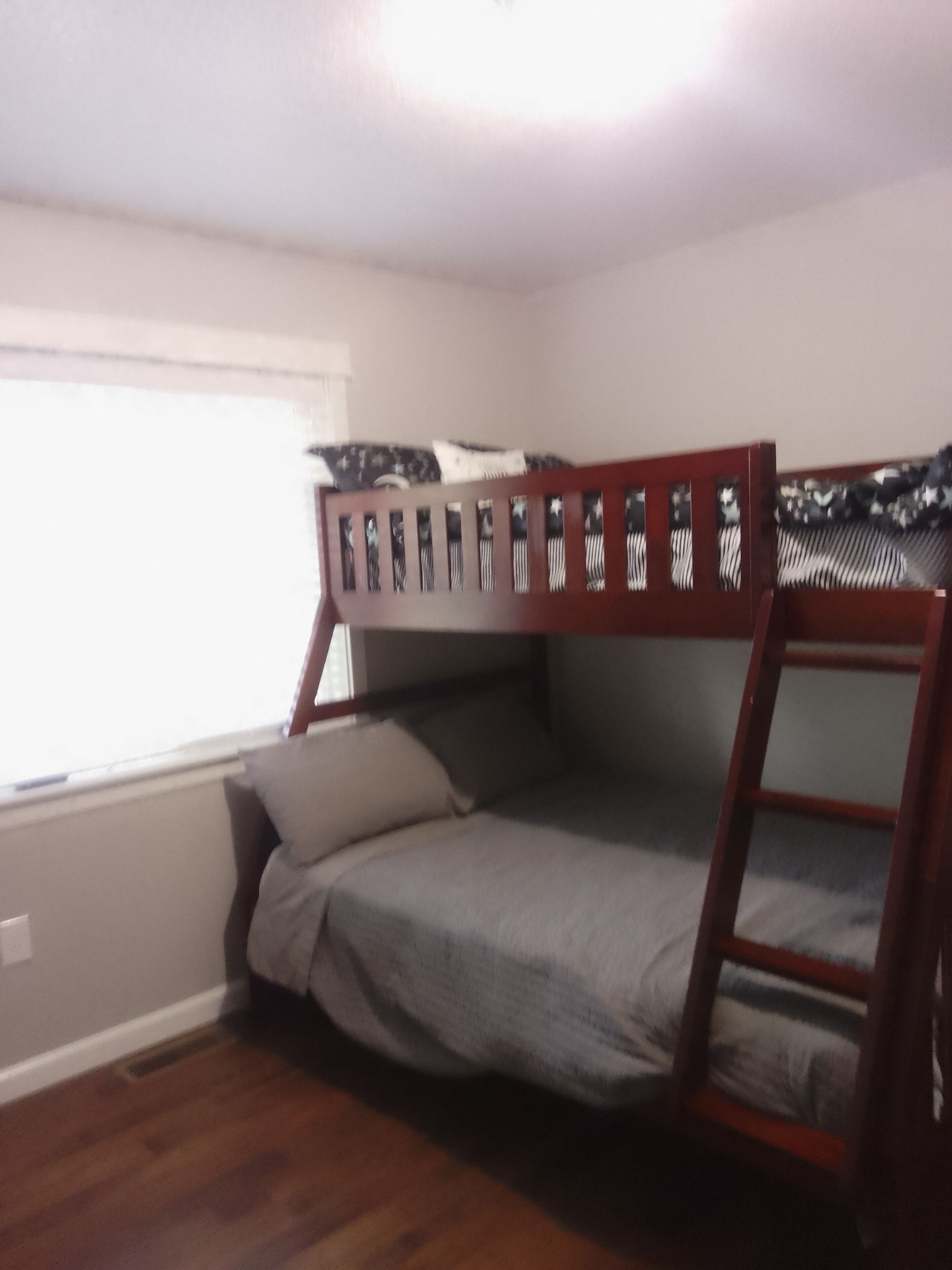 A bunk bed with a wooden frame and gray bedding in a room with hardwood flooring and a window.