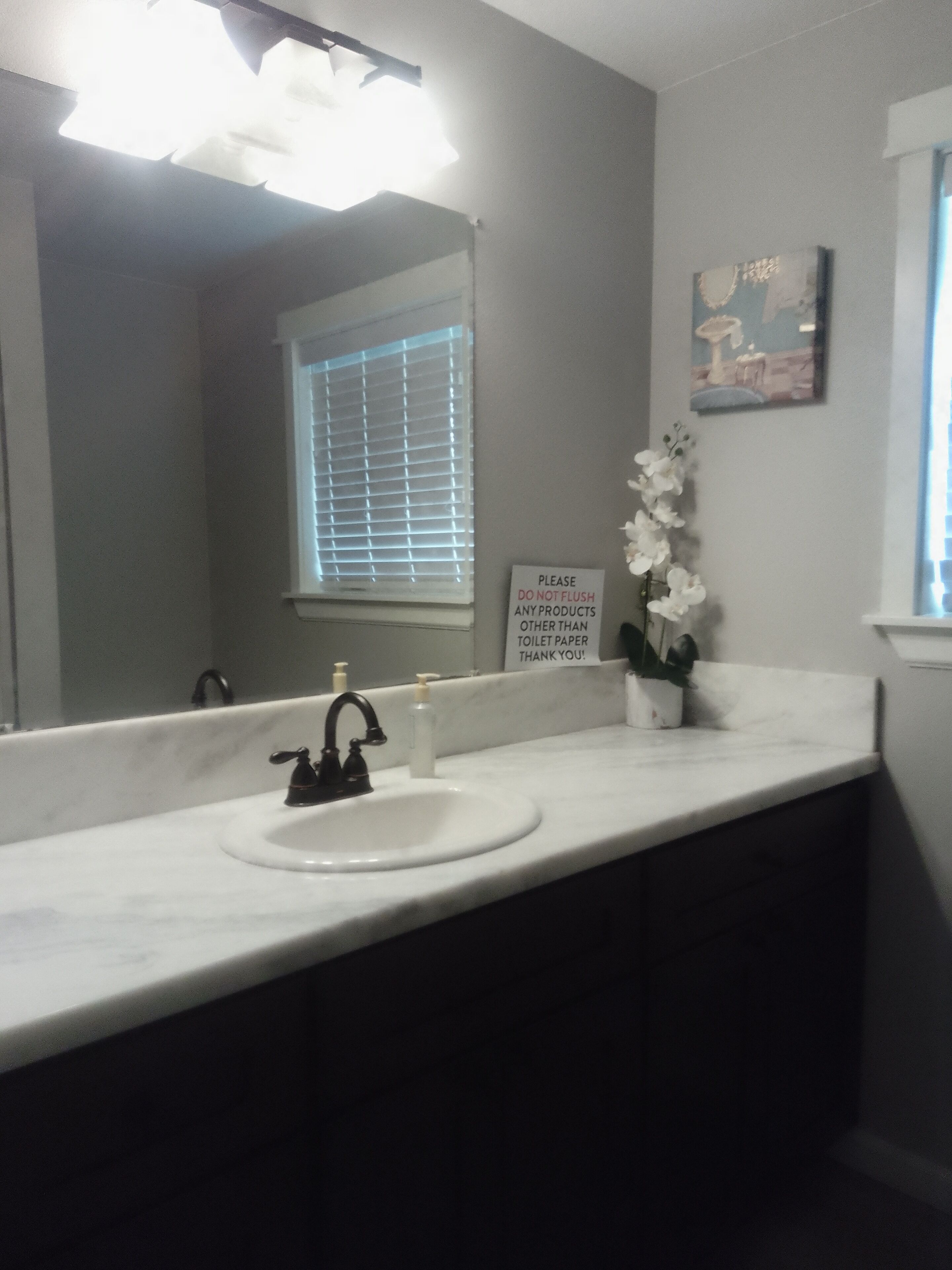 A bathroom with a white sink, black faucet, and a sign on the wall.