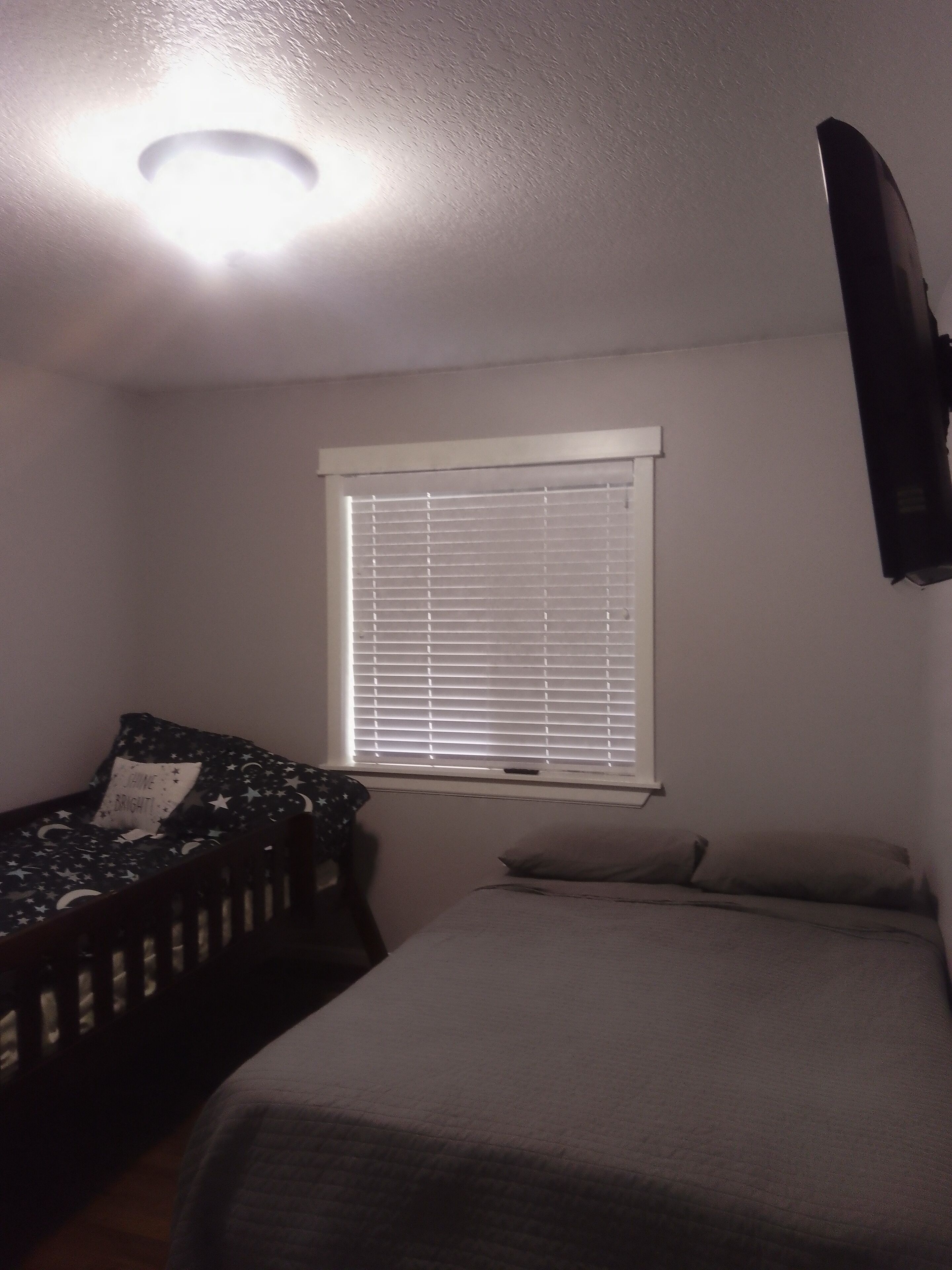 A bedroom with a bed, a nightstand, a window with blinds, and a ceiling light.