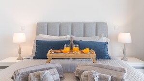 A neatly made bed with a grey headboard, two pillows, a tray with croissants and orange juice, and two bedside lamps. - Atlantic View Apartment by Atlantic Holiday (Camara de Lobos)