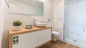 A modern bathroom with a wooden vanity, a white sink, a glass shower enclosure, and a mirror above the vanity. - Atlantic View Apartment by Atlantic Holiday (Camara de Lobos)