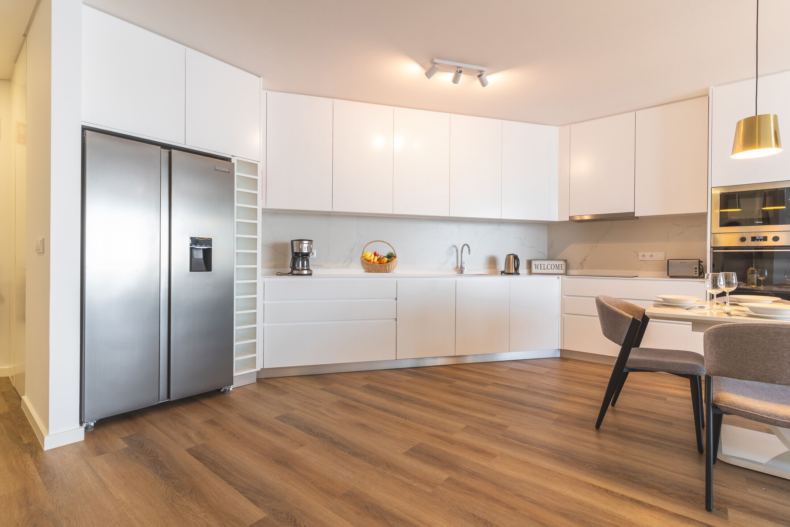 A modern kitchen with white cabinetry, stainless steel appliances, and a wooden floor.