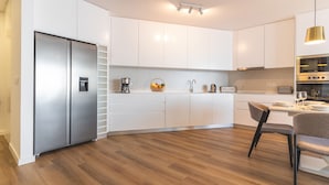 A modern kitchen with white cabinetry, stainless steel appliances, and a wooden floor. - Atlantic View Apartment by Atlantic Holiday (Camara de Lobos)