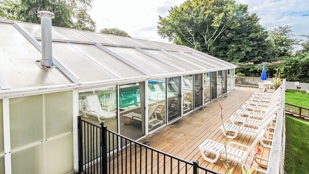 Een overdekt terras buiten, met glazen wanden, houten vloer en lounge fauteuils.