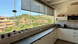 A kitchen with a view of a residential area, a window with blinds, and a microwave.