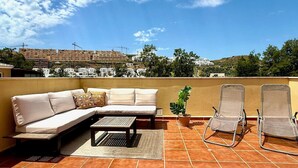 A rooftop terrace with a sofa, chairs, and a small table.