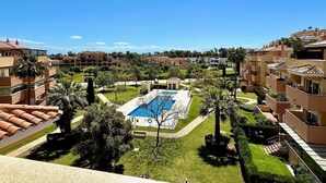 A residential area with a central swimming pool surrounded by well-maintained lawns and palm trees.