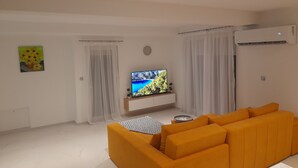 Una sala de estar moderna con un sofá grande color naranja, un televisor de pantalla plana sobre un mueble de madera y un cuadro en la pared.