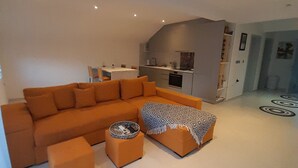 Una sala de estar moderna con un sofá seccional naranja grande, un pequeño otoman y un plaid estampado.