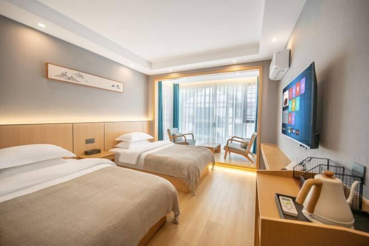Una camera d'albergo con due letti, una televisione, una scrivania con una lampada e una finestra con tende.