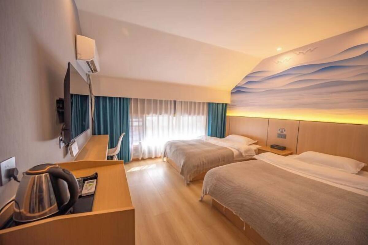 Una camera d'albergo con due letti, una scrivania con un bollitore, uno specchio e un affresco sulla parete.