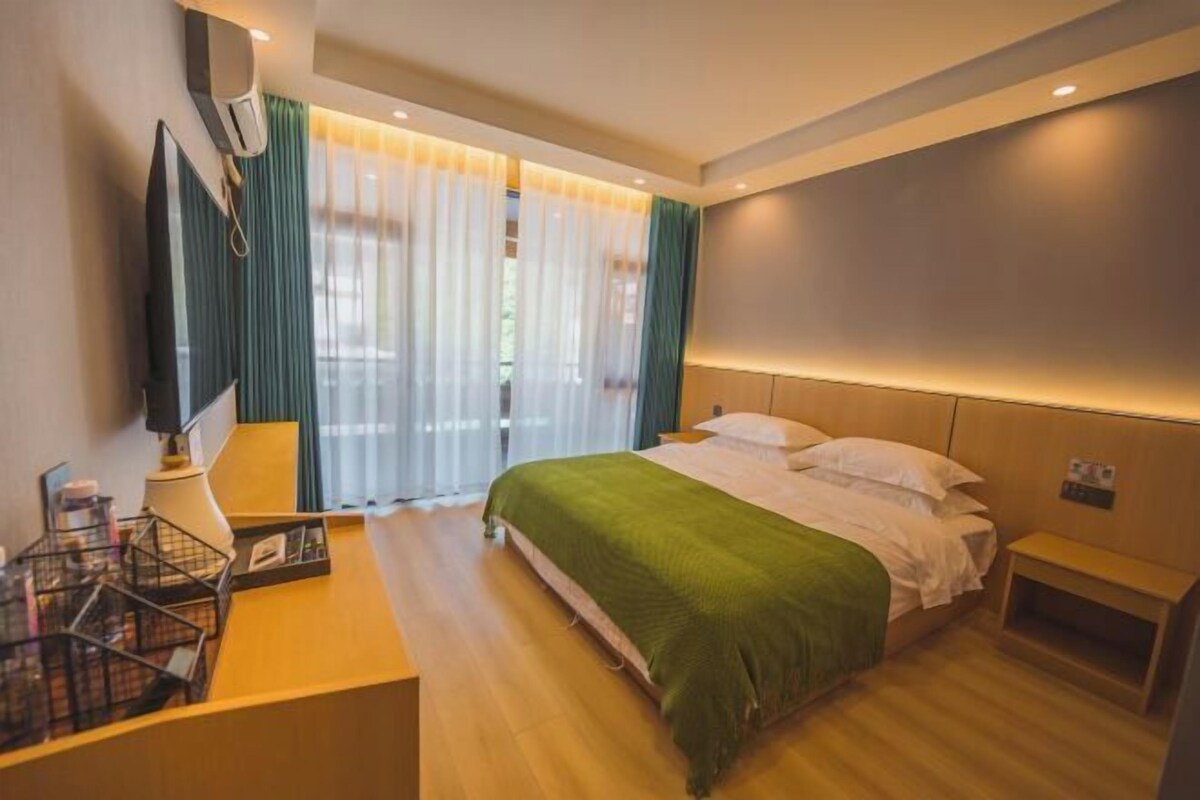 Ein modernes Hotelzimmer mit einem Bett, einem Schreibtisch mit Lampe, einem Fernseher und einem Fenster mit Vorhängen.