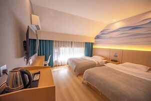 A hotel room with two beds, a desk with a kettle, a mirror, and a wall with a wave design.