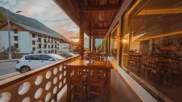 A restaurant with outdoor seating, a view of the street, and a mountain in the background.