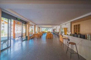 Un couloir d’hôtel avec un coin bar sur la droite, des espaces aménagés pour s’asseoir et une vue sur l’extérieur.