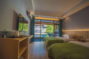 Ein Hotelzimmer mit zwei Betten, einem Schreibtisch und einem großen Fenster mit Blick auf Grünflächen und ein Gebäude.
