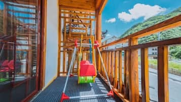 A balcony with a wooden railing, a red and green chair, and a metal structure.