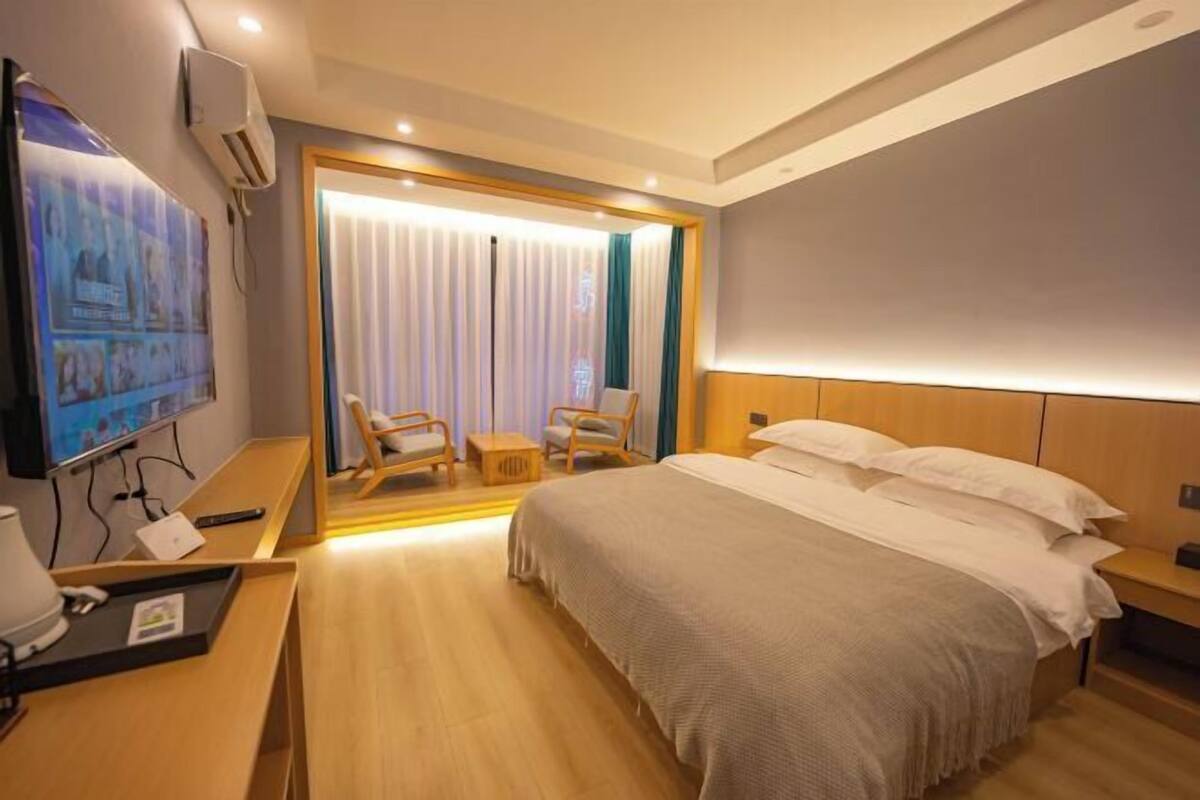 Una camera d'albergo con un letto grande, una scrivania con un computer, una televisione e un angolo salotto con sedie e un tavolo.