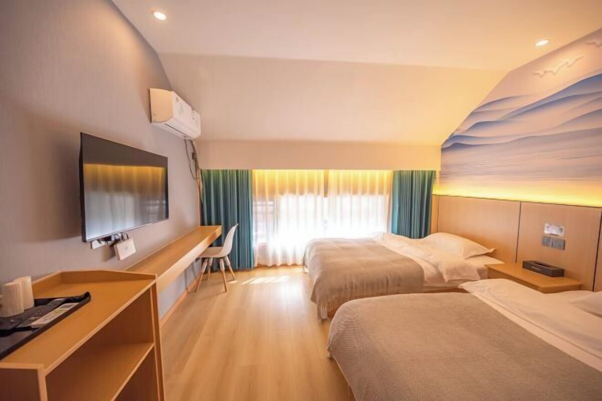 Ein Hotelzimmer mit zwei Betten, einem Schreibtisch, einem Fernseher und einer Wandklimaanlage.