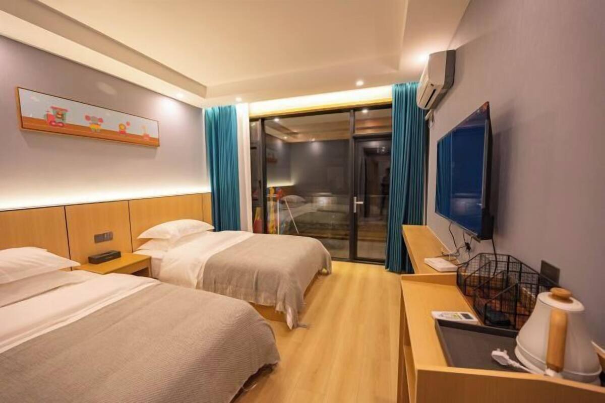 Una camera d'albergo con due letti, una televisione, una scrivania con un bollitore e una porta scorrevole in vetro che dà sul bagno.