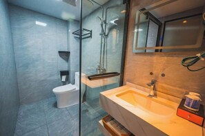 Ein modernes Badezimmer mit Duschkabine aus Glas, einer weißen Toilette und einem beige gefärbten Waschbecken mit Spiegel darüber.