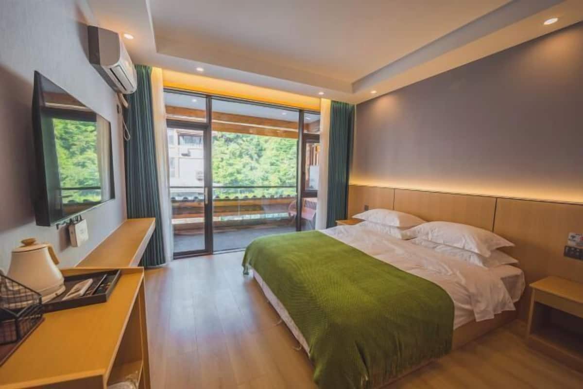 Camera d'hotel moderna con un letto grande, una scrivania e un balcone con vista sul verde.