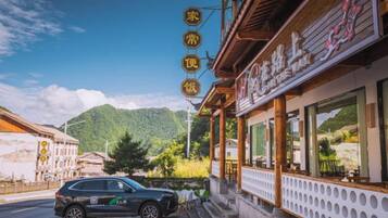 A building with a signboard, a parked car, and a mountain in the background.