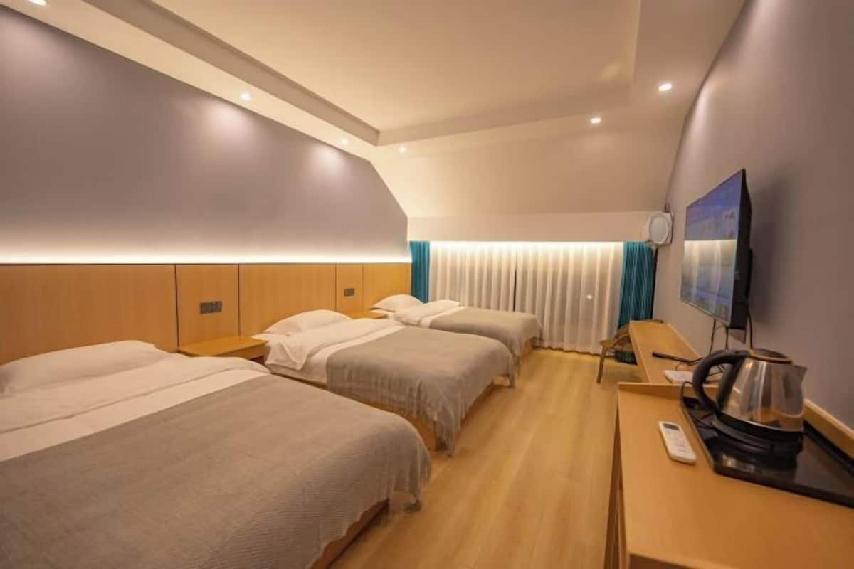Una camera d'albergo con tre letti, una scrivania in legno, un bollitore e una televisione.