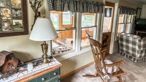 Een gezellige woonkamer met een groen kastje, een schommelstoel en een raam met ruitgordijnen.